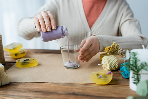 Cropped view of craftswoman pouring wax in glass near handmade candles at home