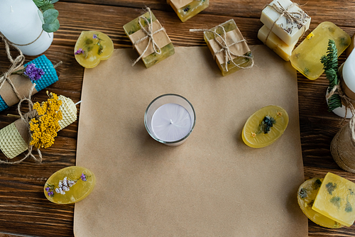 Top view of handmade candles and soap bars on craft paper on wooden surface