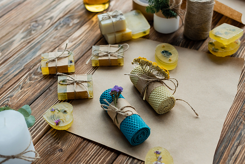 High angle view of handmade candles with flowers on craft paper near soap on wooden surface