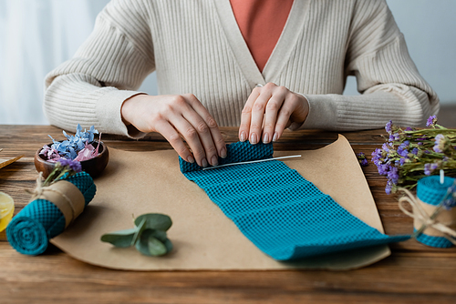 Cropped view of craftswoman making candle near flowers on craft paper at home