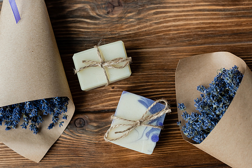 Top view of handmade soap near bouquets of lavender on wooden surface