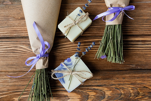 Top view of handmade soap bars near bouquets on wooden surface