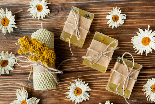 Top view of craft candle and soap near dry flowers on wooden surface