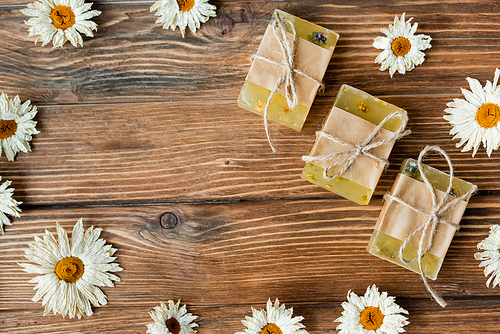 Top view of handmade soap bars in frame from dry chamomiles on wooden surface