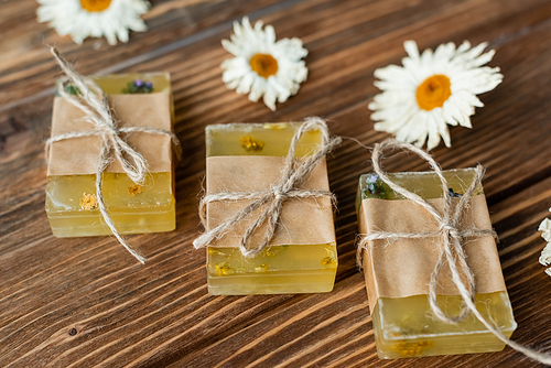 Close up view of handmade soap bards near blurred dry chamomile flowers on wooden surface