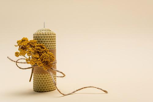 Handmade candle with dry flower and twine on beige background