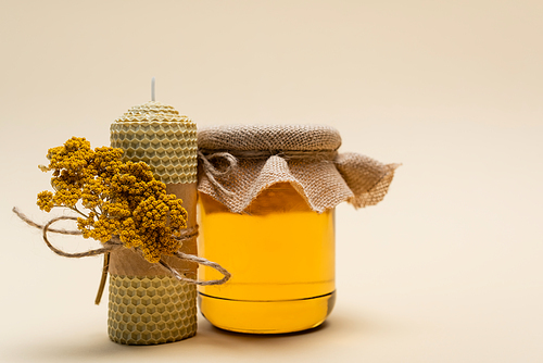 Jar with honey near handmade candle on beige background