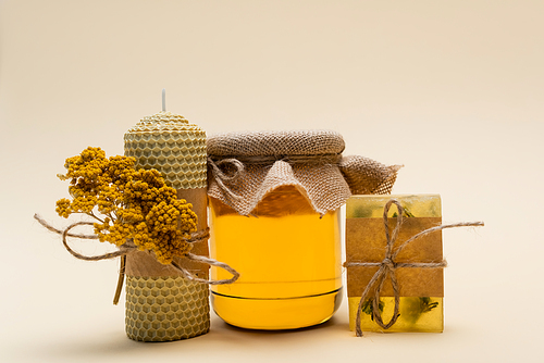 Jar of honey near handmade candle and soap on beige background