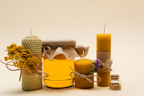 Craft candles with dry flowers and jar with honey on beige background