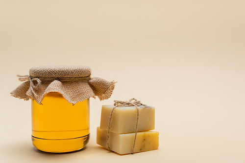 Jar with honey near handmade soap on beige background