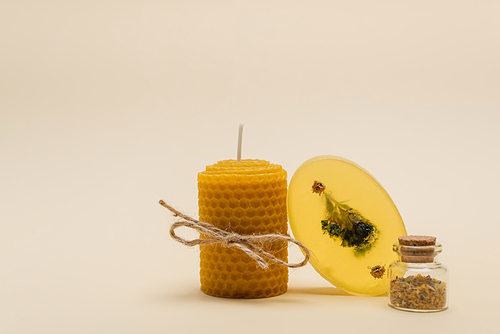 Homemade candle with twine near soap bar and jar with herbs on beige background