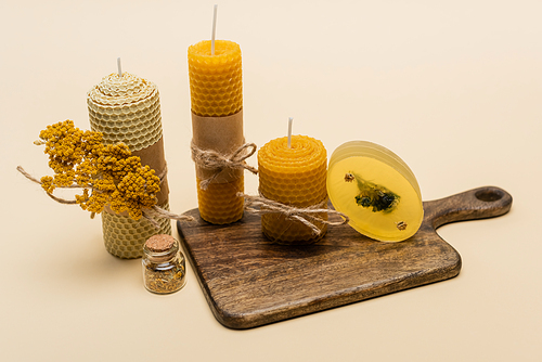 Handmade candles and soap with flowers on cutting board on beige background