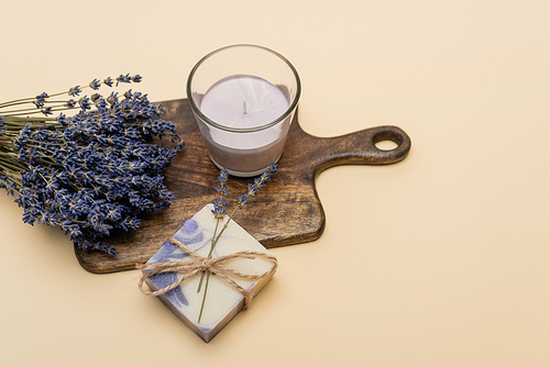 Top view of lavender near handmade soap and candle on cutting board on beige background