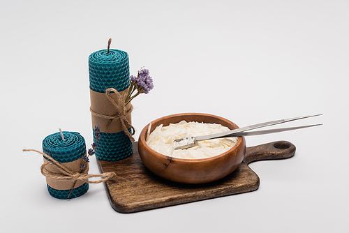 Craft candles with dry flowers near wax in wooden bowl on grey background