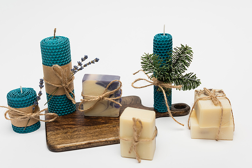 Craft candles near soap bars with twine on cutting board on grey background