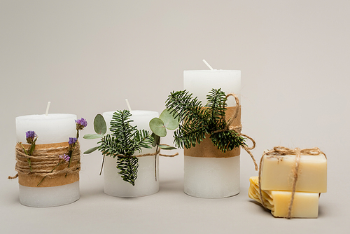 Handmade candles with plants near blurred soap bars on beige background