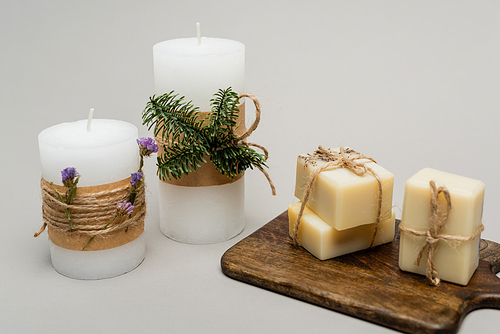 Candles with plants and soap bars on cutting board on grey background