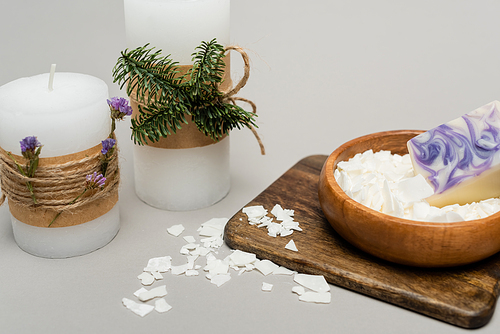 Craft candles with plants near dry wax on wooden board on grey background