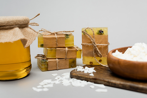 Handmade soap near blurred wax and jar with honey on cutting board on grey background