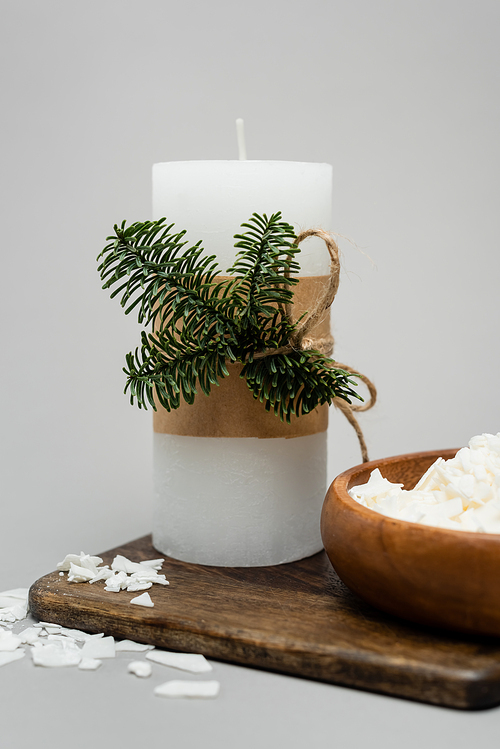 Close up view of craft candle near dry wax on wooden board on grey background