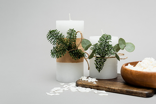 Beeswax flakes near handmade candles with plants on grey background