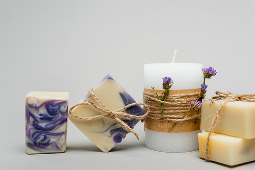 Handmade soap near candle with flowers on grey background