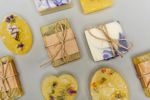 Top view of handmade soap bars with flowers and twine on grey background