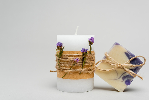 Handmade soap bar with twine near candle with flowers on grey background