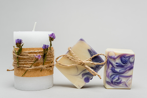 Craft soap near candle with lavender flowers on grey background