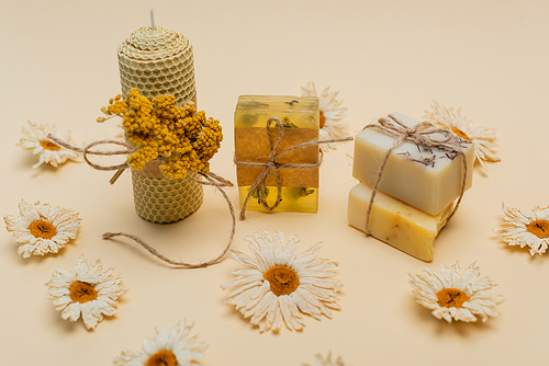 Craft soap bars near candle and dry flowers on beige background