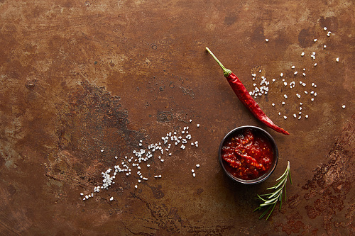 Top view of tomato sauce in bowl with chili pepper, rosemary and salt on stone surface