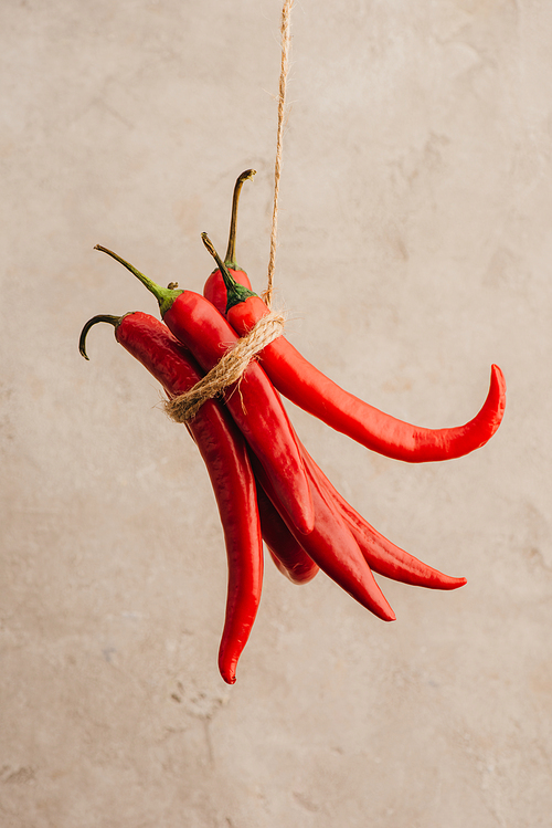 bunch of red chili peppers tied with rope hanging on beige concrete background