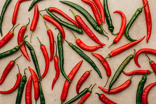 top view of red chili peppers and green jalapenos on beige concrete surface