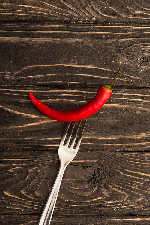 top view of spicy red chili pepper on fork on wooden surface