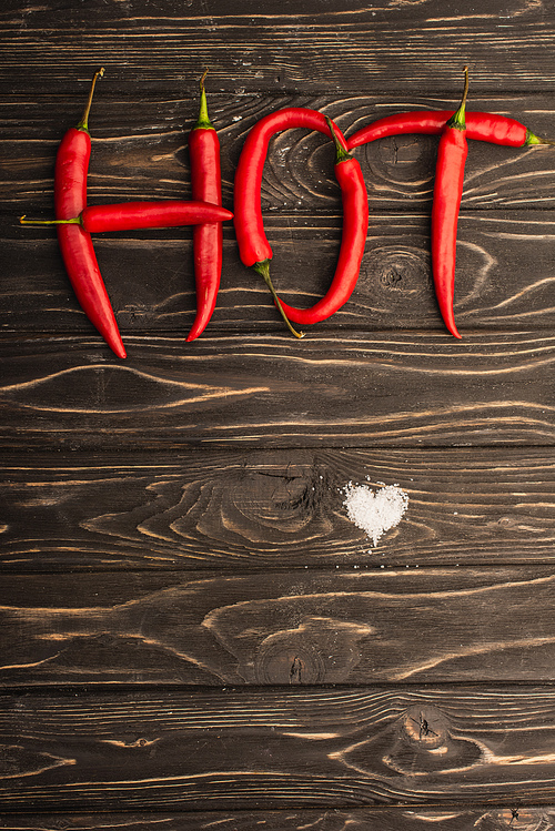 top view of word hot made of chili peppers near salt heart on wooden surface