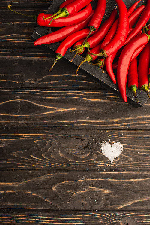 top view of chili peppers in box near salt heart on wooden surface