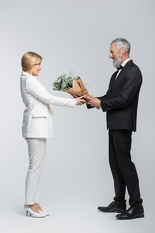 Side view of mature groom giving flowers to bride on grey background