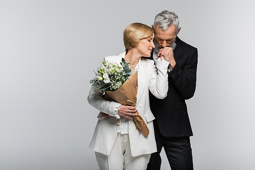 Mature groom  hand of bride in suit hold wedd bouquet isolated on grey