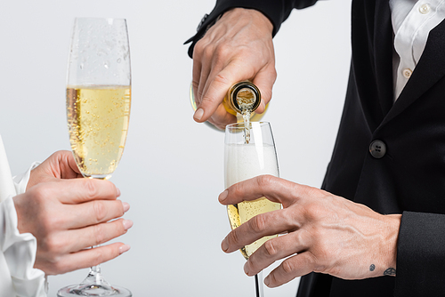 Cropped view of groom pouring champagne near bride with glass isolated on grey