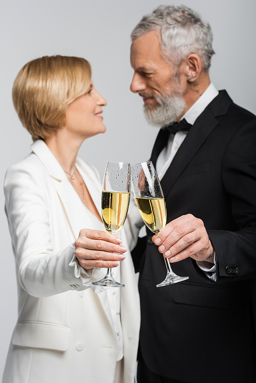 Side view of blurred mature couple in wedding clothes clinking champagne isolated on grey