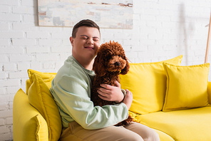 Happy teenager with down syndrome hugging poodle on couch