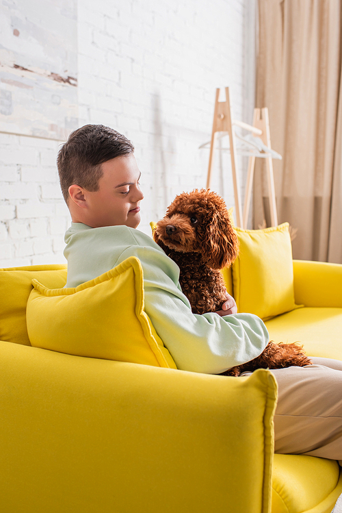 Teenager with down syndrome looking at brown poodle in living room