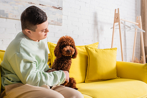 Teenager with down syndrome looking at poodle on couch at home