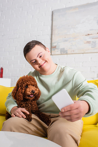 Smiling teenager with down syndrome taking selfie with poodle at home