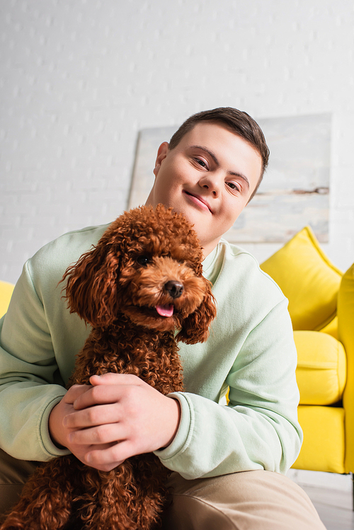 Teen boy with down syndrome hugging poodle and  in living room