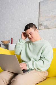 Teenager with down syndrome using laptop on couch in living room