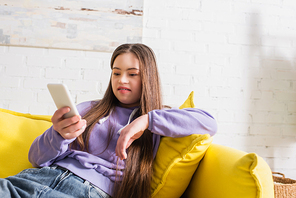 Smiling teenager with sown syndrome using blurred mobile phone on couch at home