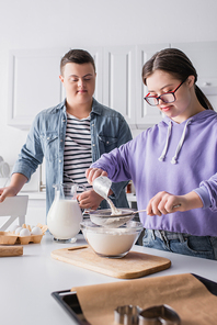 Teenager with down syndrome cooking near food and friend in kitchen