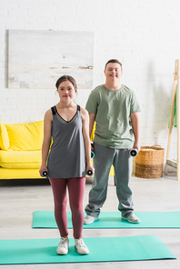 Teen friends with down syndrome holding dumbbells on fitness mats at home