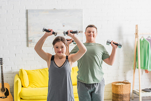 Teenager with down syndrome working out with dumbbells near blurred friend at home